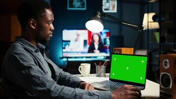 Teleworker at home editing documents next to mockup on his laptop, submitting reports and files before deadline. Black freelancer managing digital paperwork within the work platform. Camera A. video