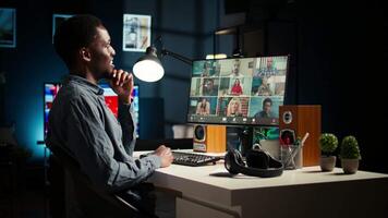 Black guy meeting with group of individuals on web conference, uses technology for virtual communication. Freelancer working remotely, online meetings or classes in a cozy home. Camera A. video