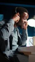 Vertical Young focused freelancer attending an online meeting from his home office, discussing with associates remotely. Smiling black man engages in virtual communication, remote technology. Camera A. video