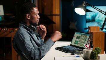 Financial manager doing remote accounting work with music on headset, solving his tasks on laptop at home. African american guy multitasking with his favorite playlist to help him focus. Camera B. video