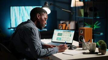 Black man organizing his schedule with a planner and putting a reminder, creating an adhesive note post it and browsing the web. Modern productive guy writes a memo for research. Camera B. video