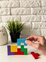 Female hand assembling wooden cube puzzle on white background with potted plant in background. photo