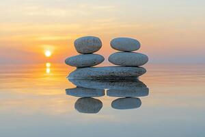 Large smooth stones stand in two stacks on a mirror-like water surface against a calm sky. The concept of balance and peace of mind. photo