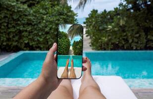 The girl holds the phone and takes pictures of her legs against the background of the pool. Point of view. photo