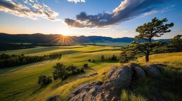 Sunset over a peaceful mountain valley with rolling green meadows, trees, and rocky outcrops photo
