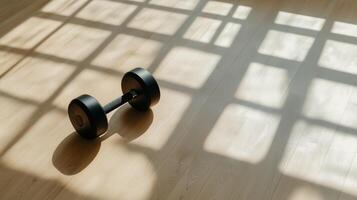 Minimalist gym scene with a single black dumbbell and window shadows on a wooden floor photo