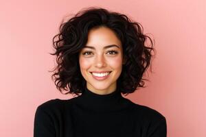 Portrait of a smiling woman with curly dark hair wearing a black sweater against a pink background photo