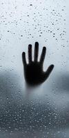Silhouette of a Hand on a Rainy Glass Window with Droplets Creating a Mysterious Atmosphere photo