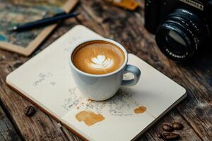 Cup of latte art coffee placed on an open notebook with camera and rustic table background photo