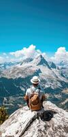 Traveler Sitting on Cliff with Backpack Overlooking Scenic Mountain Range and Clear Blue Sky photo