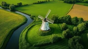 Scenic aerial view of white windmill surrounded by lush green fields and a winding river photo