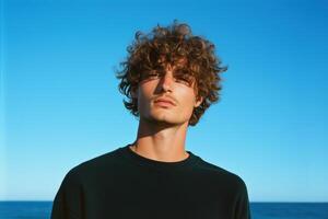 A man with curly hair standing in front of the ocean photo