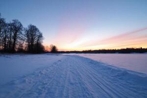 Snow-covered path leading to a serene winter sunset. photo