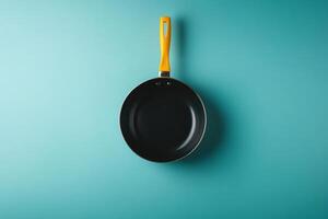 A black frying pan with a yellow handle on a turquoise background. photo