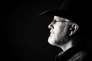 A profile of a man with a beard and hat against a dark background. photo