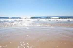 A beach with a clear blue sky and a wave photo