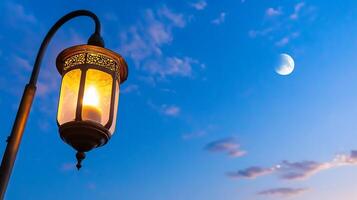A lantern illuminated against a twilight sky with a crescent moon. photo