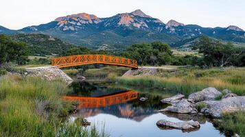Scenic Orange Footbridge Over Calm River with Majestic Mountain Range Background photo