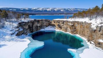 Stunning Aerial View of Frozen Turquoise Lake in Winter Snow Covered Cliffs and Mountains photo