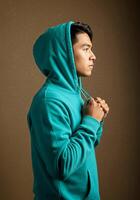 A man in a blue hoodie standing against a brown wall photo