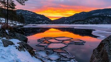 Stunning Winter Sunset Over Frozen Lake with Mountain Reflections and Ice Patterns photo