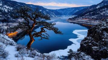Serene Winter Landscape Snow Covered Mountains Frozen Lake and Solitary Tree at Dusk photo