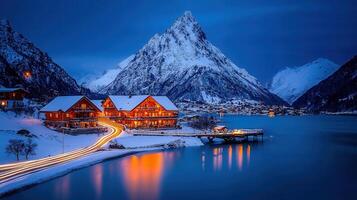 Illuminated Alpine Lodge at Dusk Snowy Mountains Lake Reflections Winter Scene photo