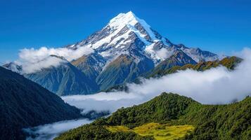 Majestic Snow Capped Mountain Peak Soaring Above Clouds and Lush Green Valley photo