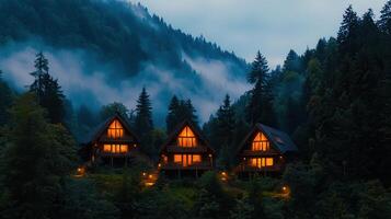 Three Illuminated Cozy Cabins Nestled in Misty Mountain Forest at Dusk photo