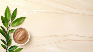 Natural Brown Face Mask Cream in Bowl with Green Leaves on Beige Marble Background photo