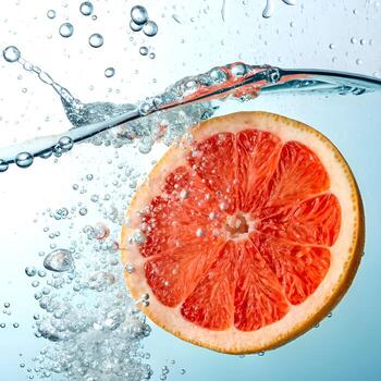 Fresh grapefruit slice splashing into water with bubbles and droplets photo