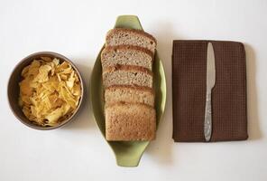 Brown bread slices with a knife and potato chips on a white background photo