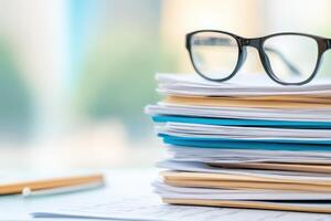 Stacked paperwork with eyeglasses resting on the top in a bright office environment during the day photo