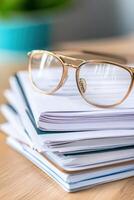 Glasses resting on a stack of organized notebooks on a wooden desk during a bright day in a cozy workspace photo