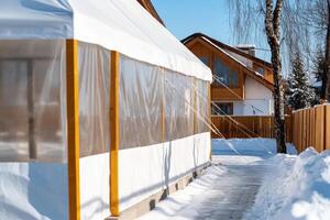 Tent structure beside snow-covered pathway leading to a wooden house in a winter setting during daylight photo