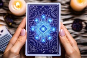 Mystical tarot card deck with glowing blue and purple patterns held in hands during candlelit spiritual session photo