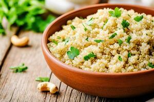Bowl of cooked quinoa topped with fresh herbs, nuts, and vegetables on a rustic wooden table photo