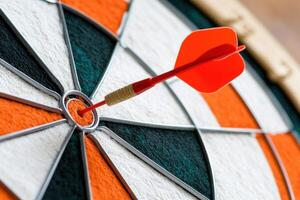 Perfectly aimed red dart striking the center of an orange and white dartboard, showcasing exceptional accuracy and the thrill of the game photo