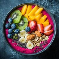 Smoothie bowl with dragon fruit puree, topped with mango, kiwi, banana, strawberries, blueberries, almonds, chia seeds, and oats vibrant and nutritious breakfast served in black bowl on dark surface photo