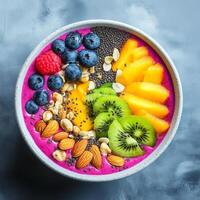 A smoothie bowl with dragon fruit puree, topped with kiwi, raspberries, blueberries, almonds, oats, and chia seeds. A nutritious and refreshing meal served in a dark bowl on a textured background photo