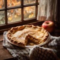 An apple pie with a crispy crust sits near a window, a slice removed to expose tender apple chunks in a caramelized filling. A red apple rests beside it on a rustic wooden surface with a linen cloth photo