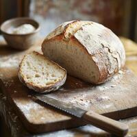 Fresh-baked loaf bread sits on a wooden cutting board, lightly covered in flour sharp knife rests beside a sliced piece, while a small bowl of salt adds a finishing touch to the rustic kitchen scene photo