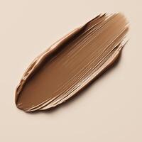 A rich, creamy brown foundation swatch with smooth, even texture on a neutral beige background. The thick application and natural sheen highlight the formulas blendability and coverage. photo