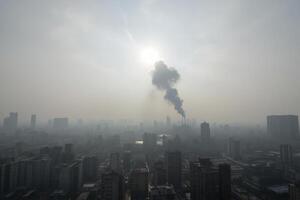 A polluted city with tall buildings and a thick layer of smog, a large plume of smoke rising from a factory, the sun shining dimly through the haze, Scene02 photo