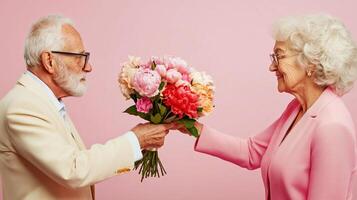 Elderly man shares a colorful bouquet with a woman in a soft pink setting during a cheerful moment of connection photo