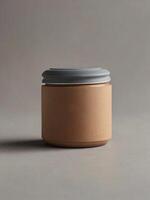 A small, cylindrical container made of brown paper sits on a gray surface. The lid is a light blue-gray color. The background is a muted gray photo