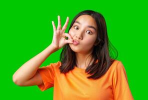 Young girl making a playful gesture against a bright green background at home during the daytime photo