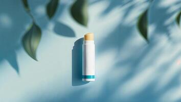 Lip balm placed on a blue surface with soft shadows and green leaves creating a calming atmosphere, showcasing beauty and self-care photo