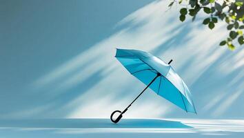 Umbrella leaning against a blue backdrop with soft shadows and green leaves in a serene setting photo