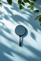 Reflective handheld mirror on a pastel blue surface with shadows from green leaves in a serene setting photo